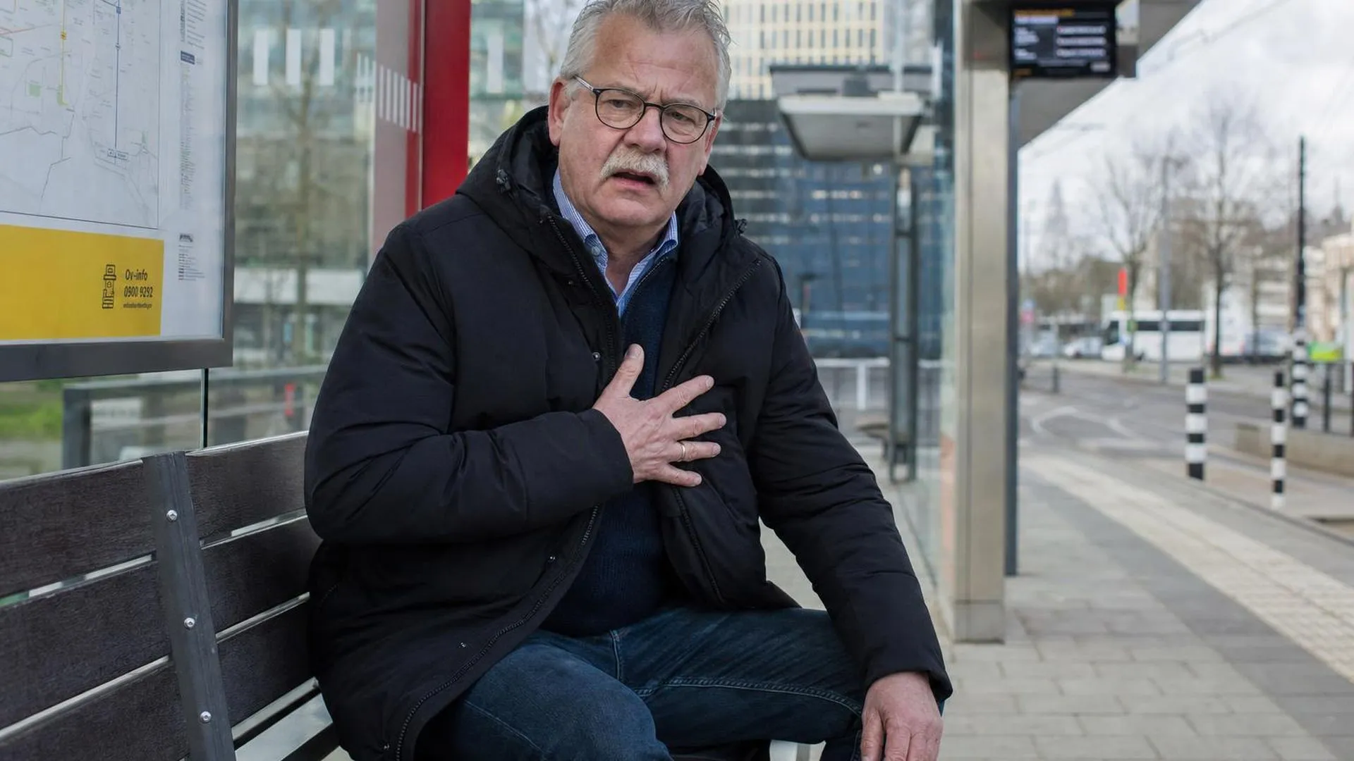 Persoon zit op een bankje op een tramstation, hand op de borst, overdonderd door een plotseling geluid