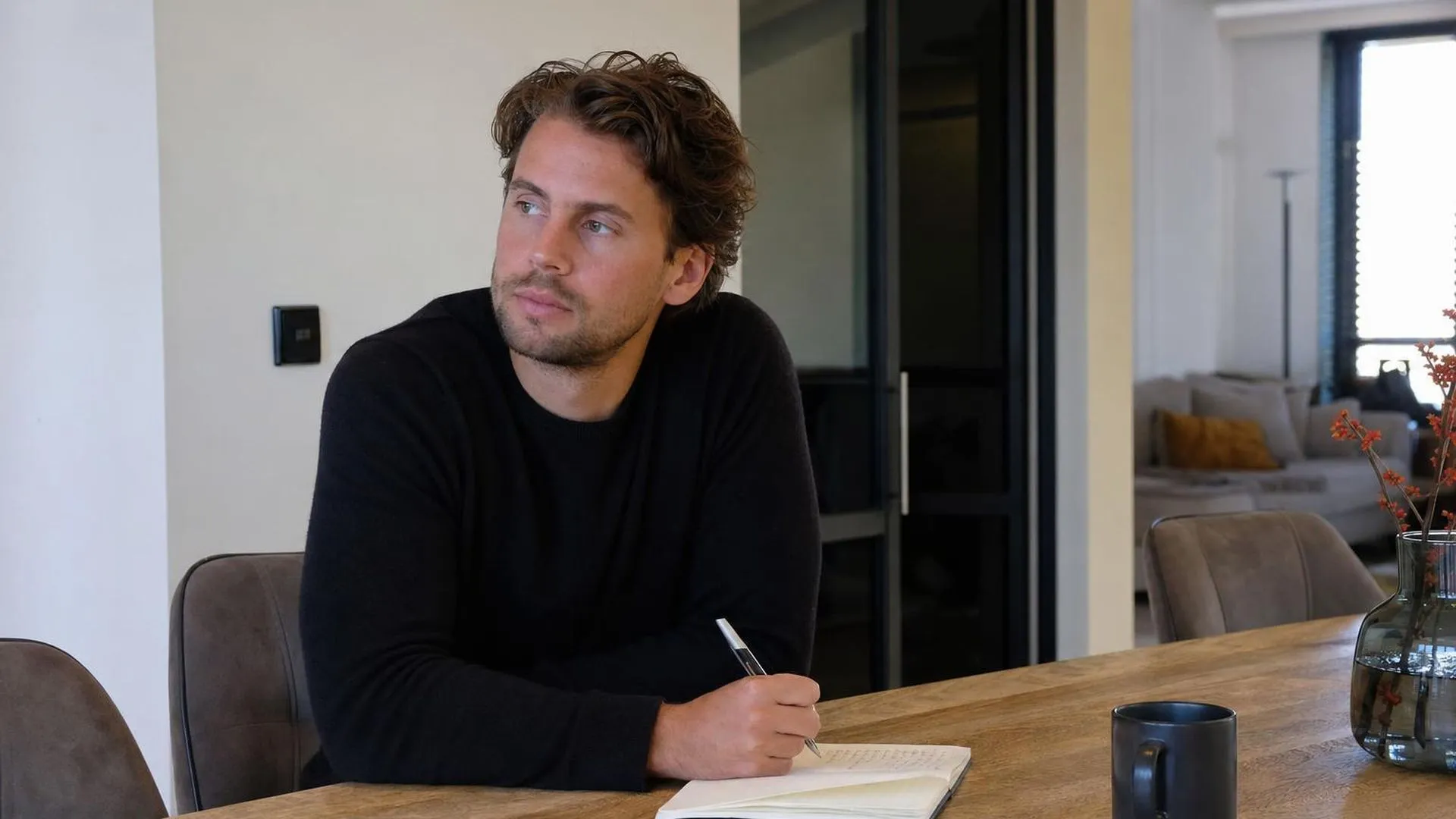 Persoon zit aan tafel en staart peinzend voor zich uit, notebook open voor hen