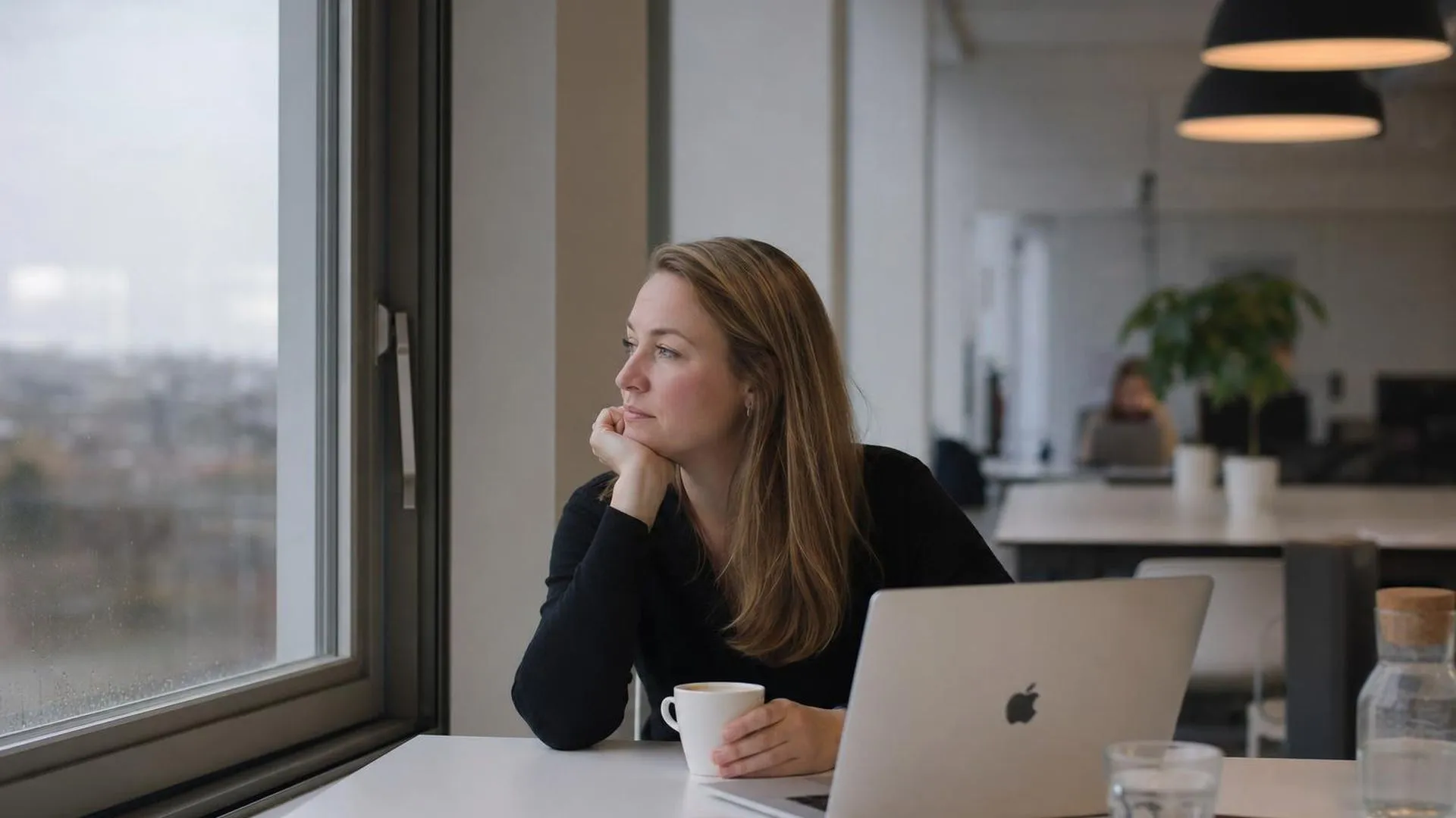 Oudere medewerker zit peinzend aan een vergadertafel met een kop koffie