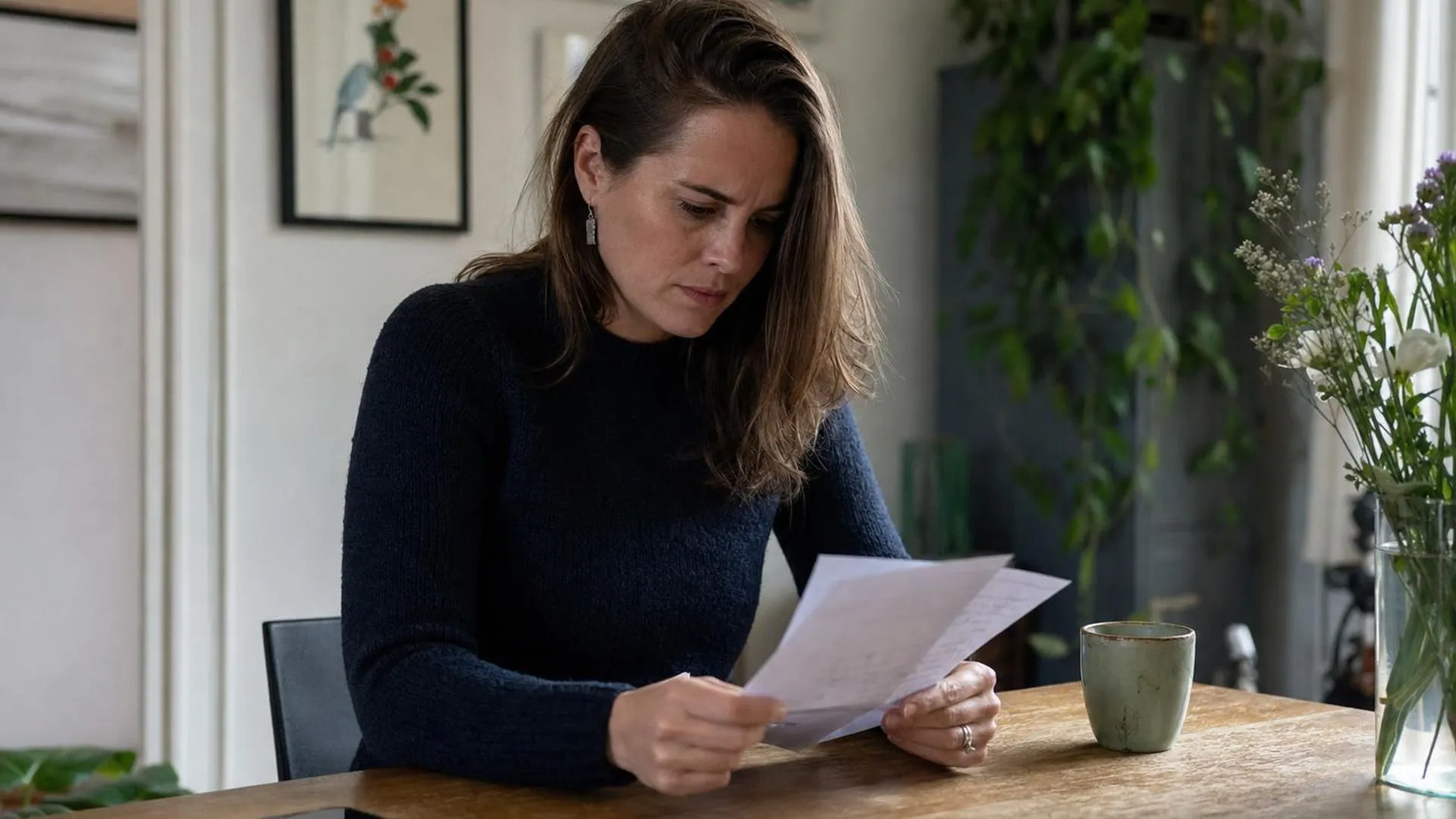 Iemand leest een brief aan de eettafel met de telefoon omgekeerd naast zich