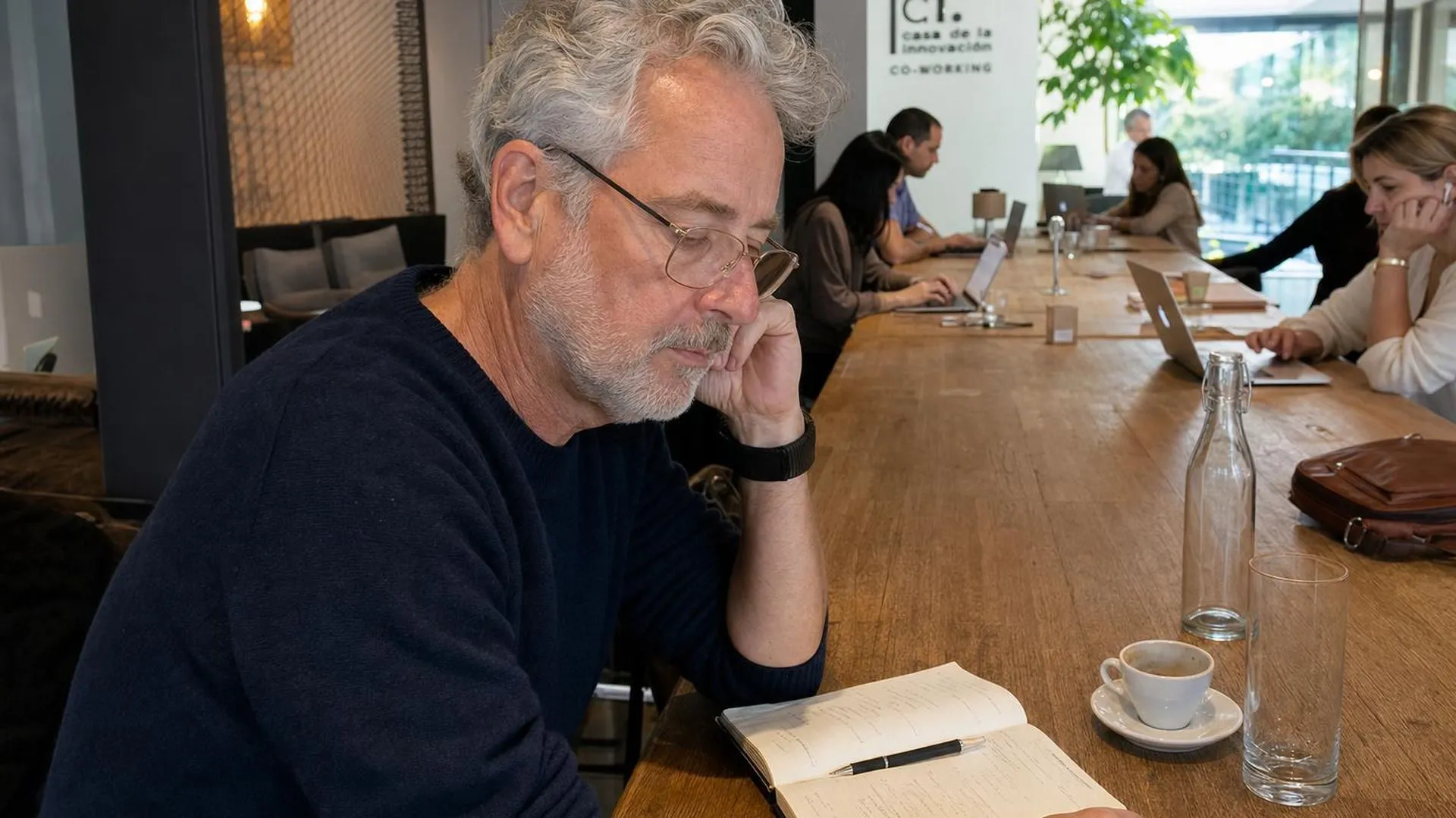 Persoon zit peinzend aan een werktafel met een open notitieboek voor zich