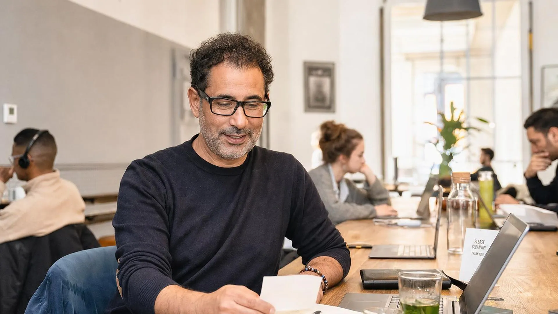 Persoon die even pauzeert en glimlacht na het lezen van een bericht aan een gedeelde werktafel