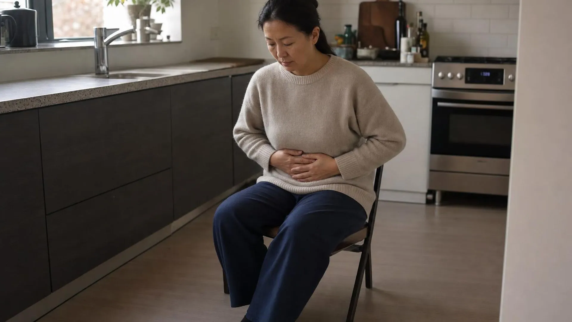 Persoon met buikpijn door stress zit aan keukentafel