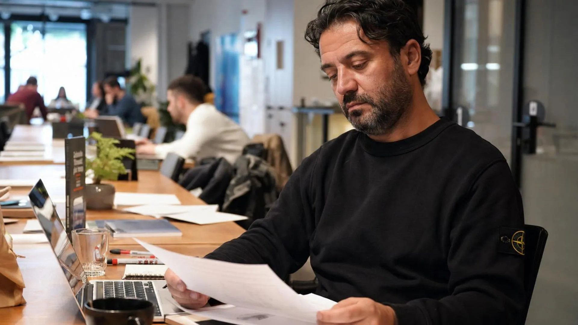 Leidinggevende kijkt peinzend naar werkdocumenten aan een gedeelde werktafel