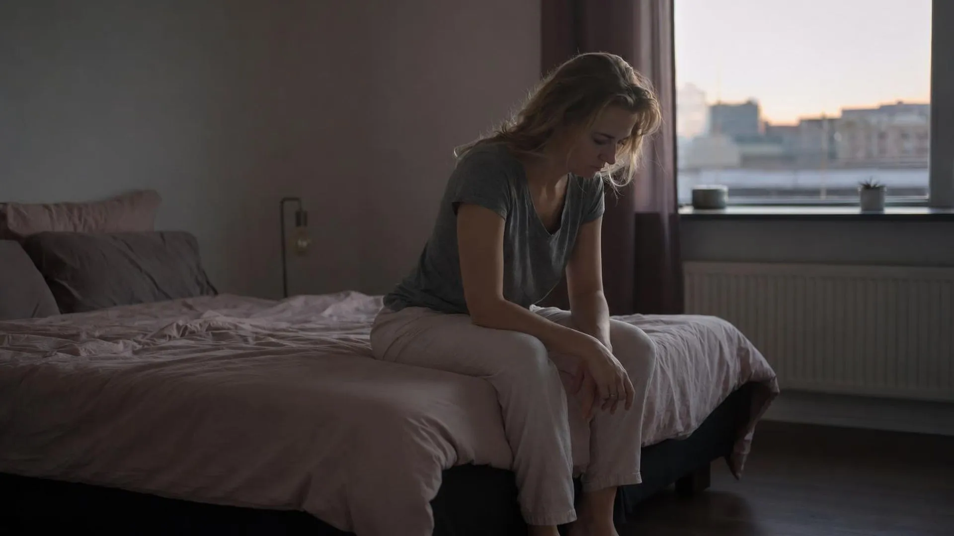 Vrouw zit uitgeput op de rand van haar bed, emotioneel leeggelopen