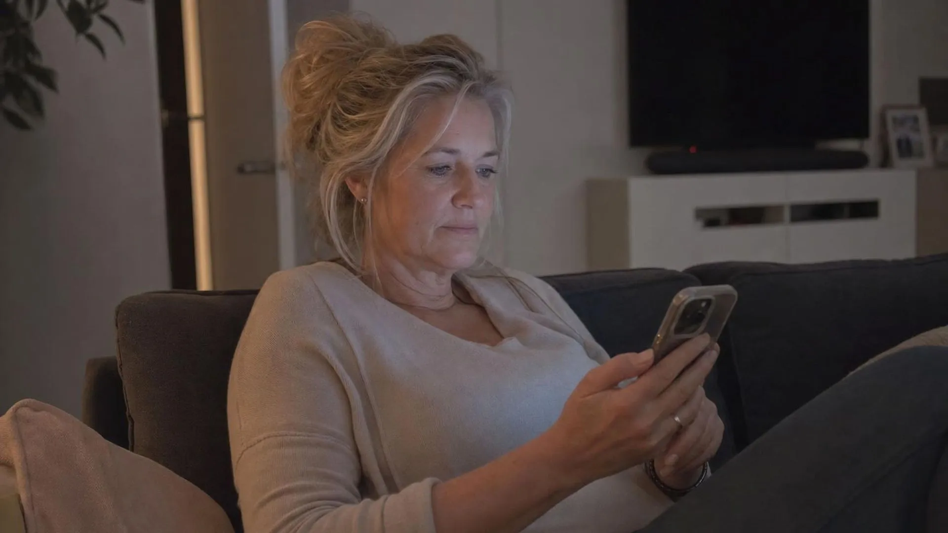 Persoon scrolt 's avonds op de bank door de telefoon met een leeg gevoel