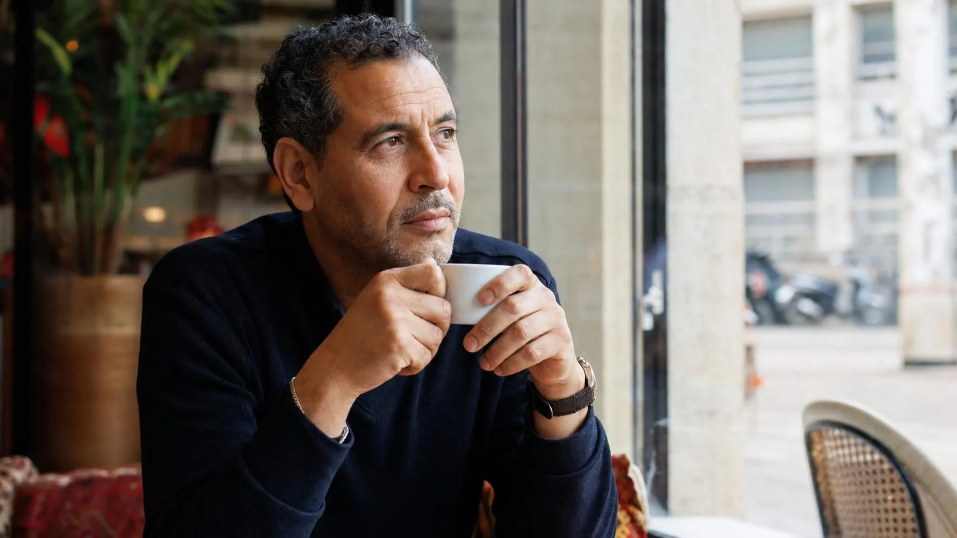 Persoon zit peinzend bij een raam in een café met een kop koffie