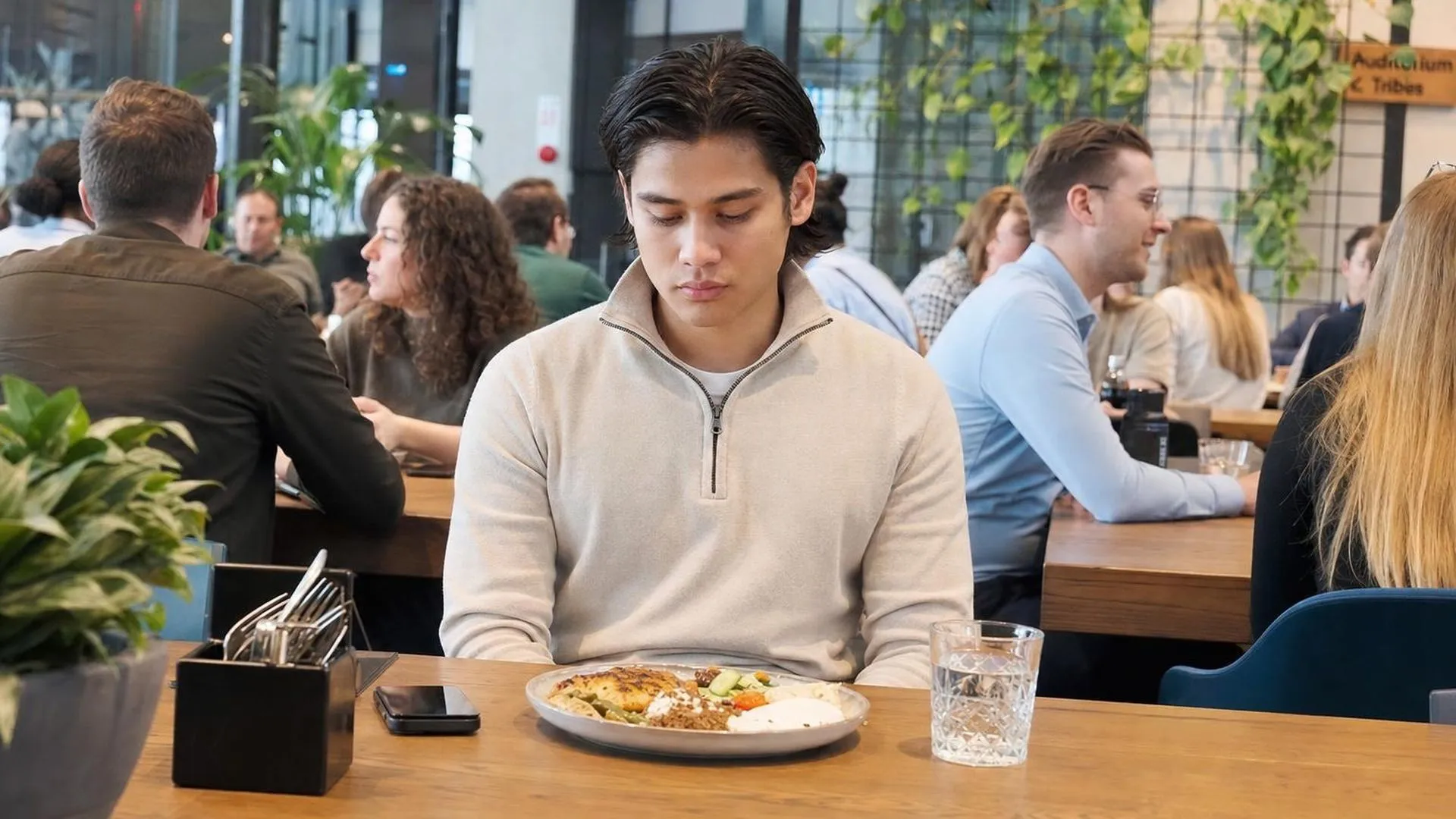 Iemand alleen aan een drukke lunchteafel, vermoeid en in gedachten verzonken