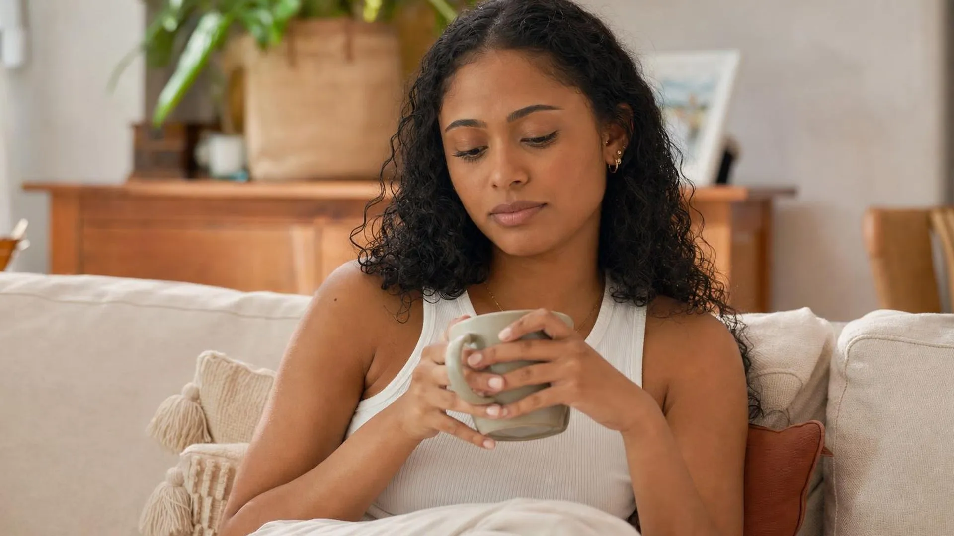 Persoon zit stil op de bank met een kop koffie, lijkt gespannen ondanks de rust om hen heen