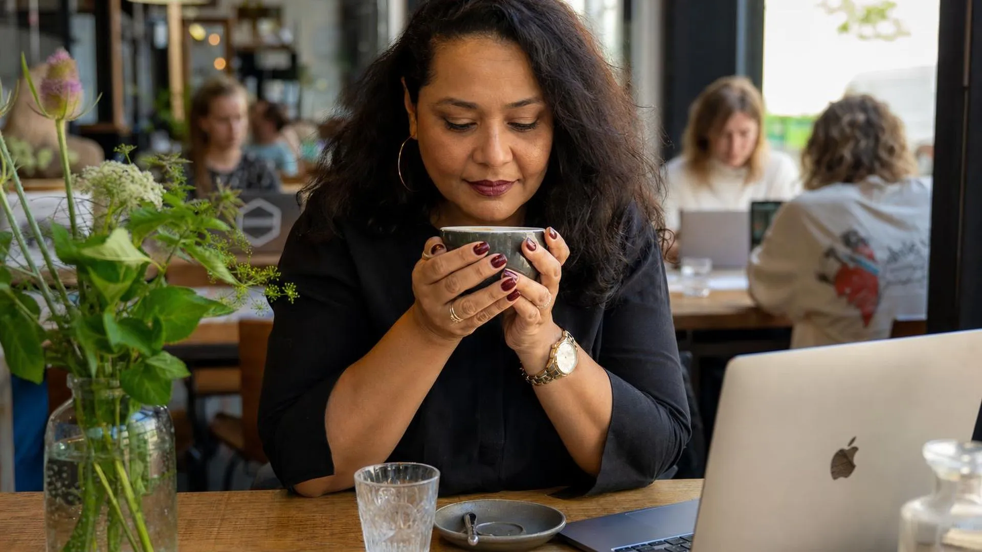 Persoon zit peinzend aan een tafel met een kop koffie in handen