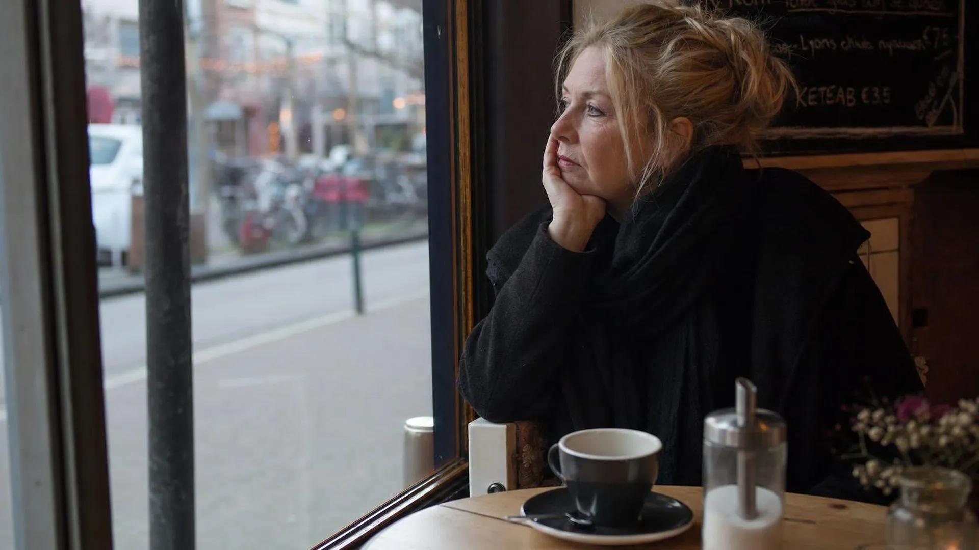 Persoon die peinzend naar buiten kijkt in een café, zich niet serieus genomen voelend