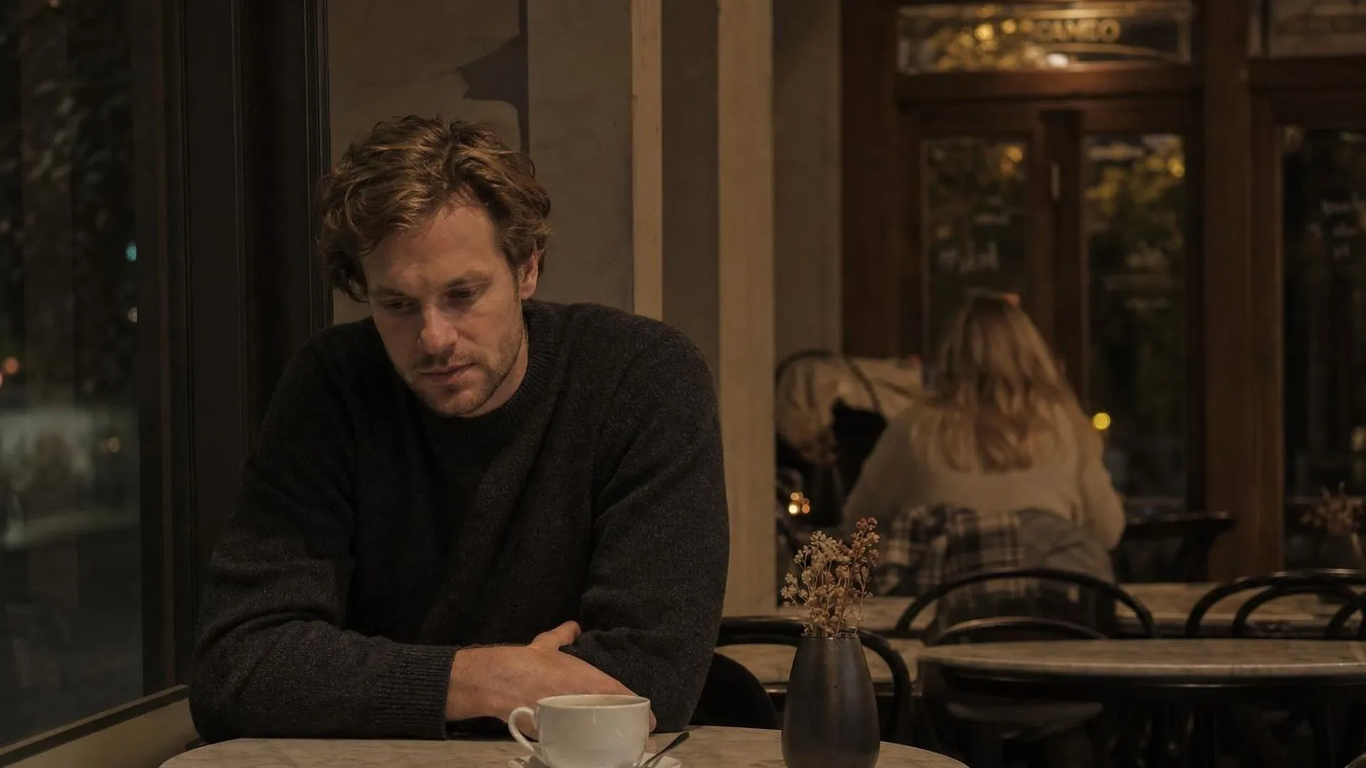 Persoon zit peinzend in een café met een onaangeroerd kopje koffie voor zich