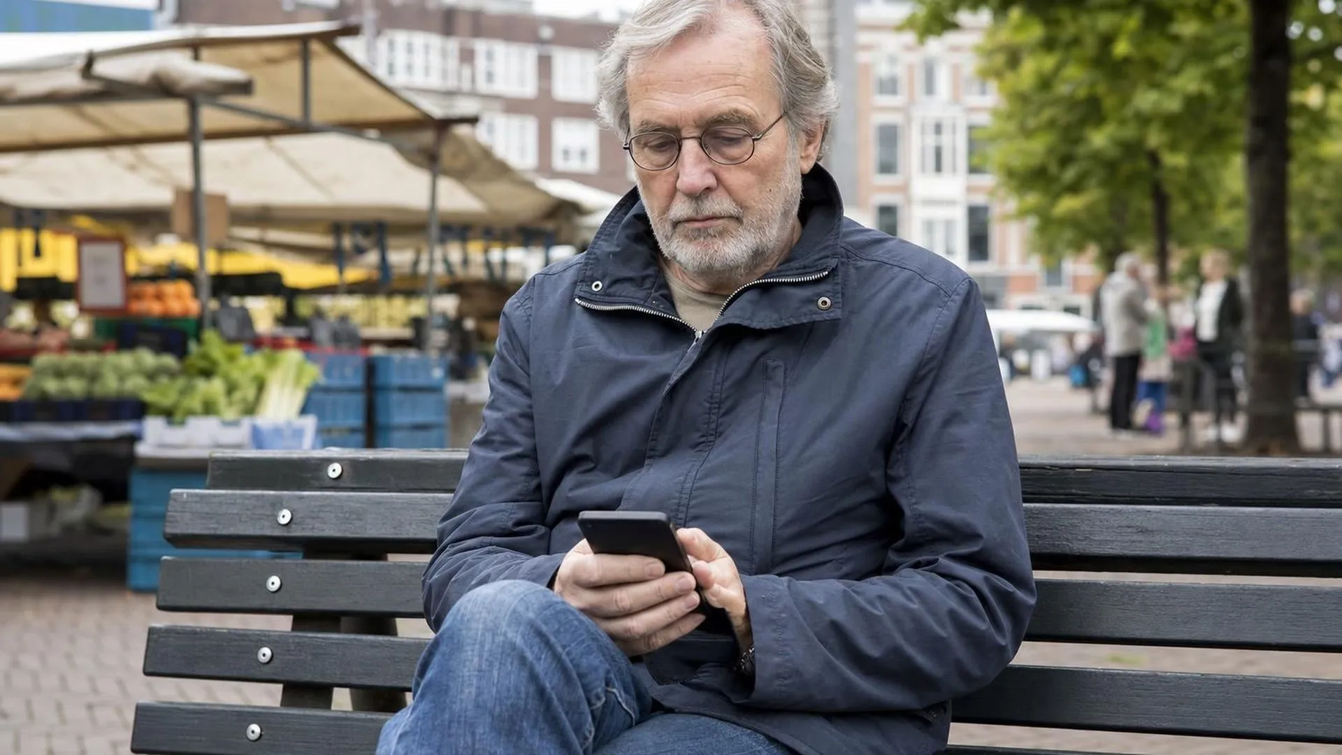 Iemand zit op een bank en kijkt met een neutrale blik naar zijn telefoon