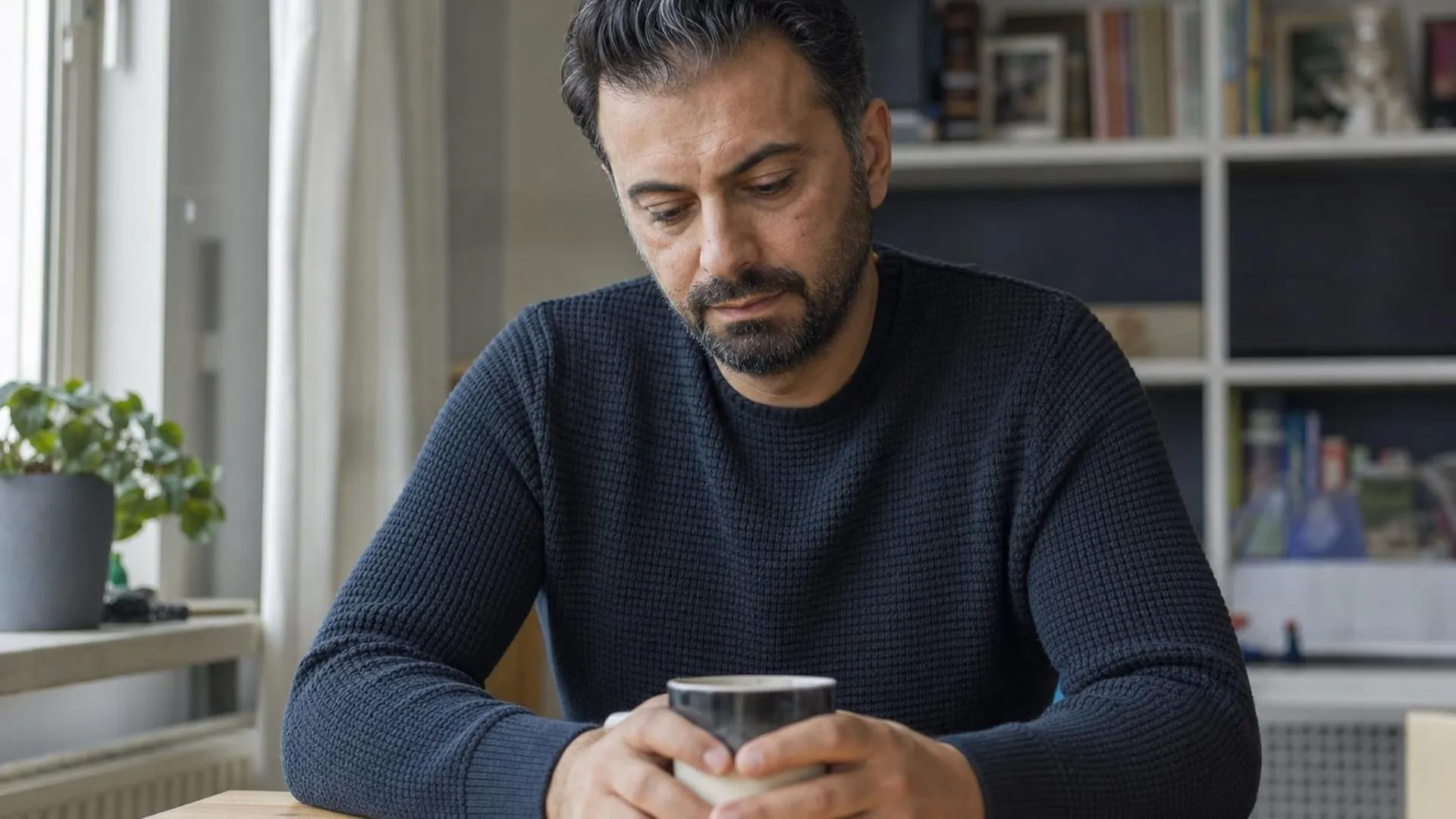 Vrouw aan tafel met mok, peinzend, in verband met stress en lichamelijke klachten