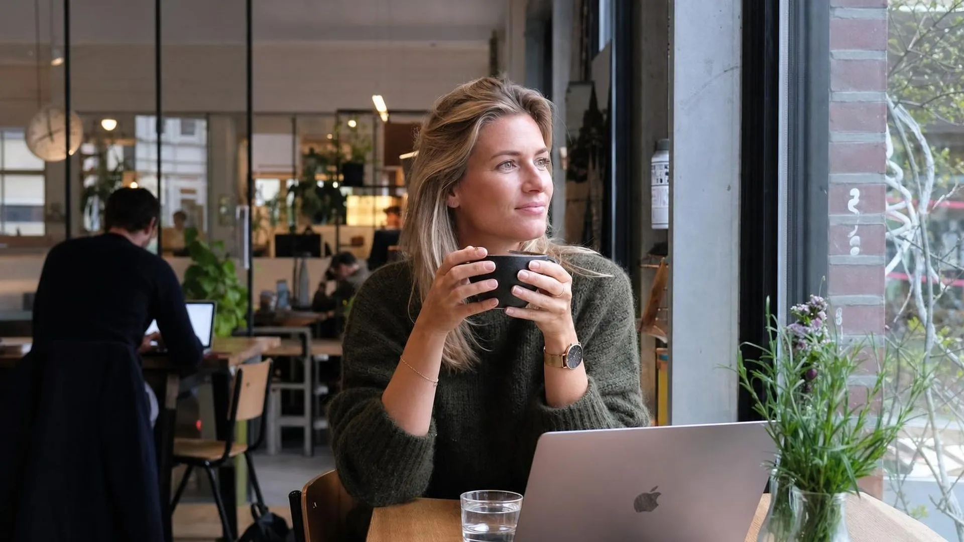 Persoon zit in een koffiebar en kijkt naar buiten, ogenschijnlijk in gedachten verzonken