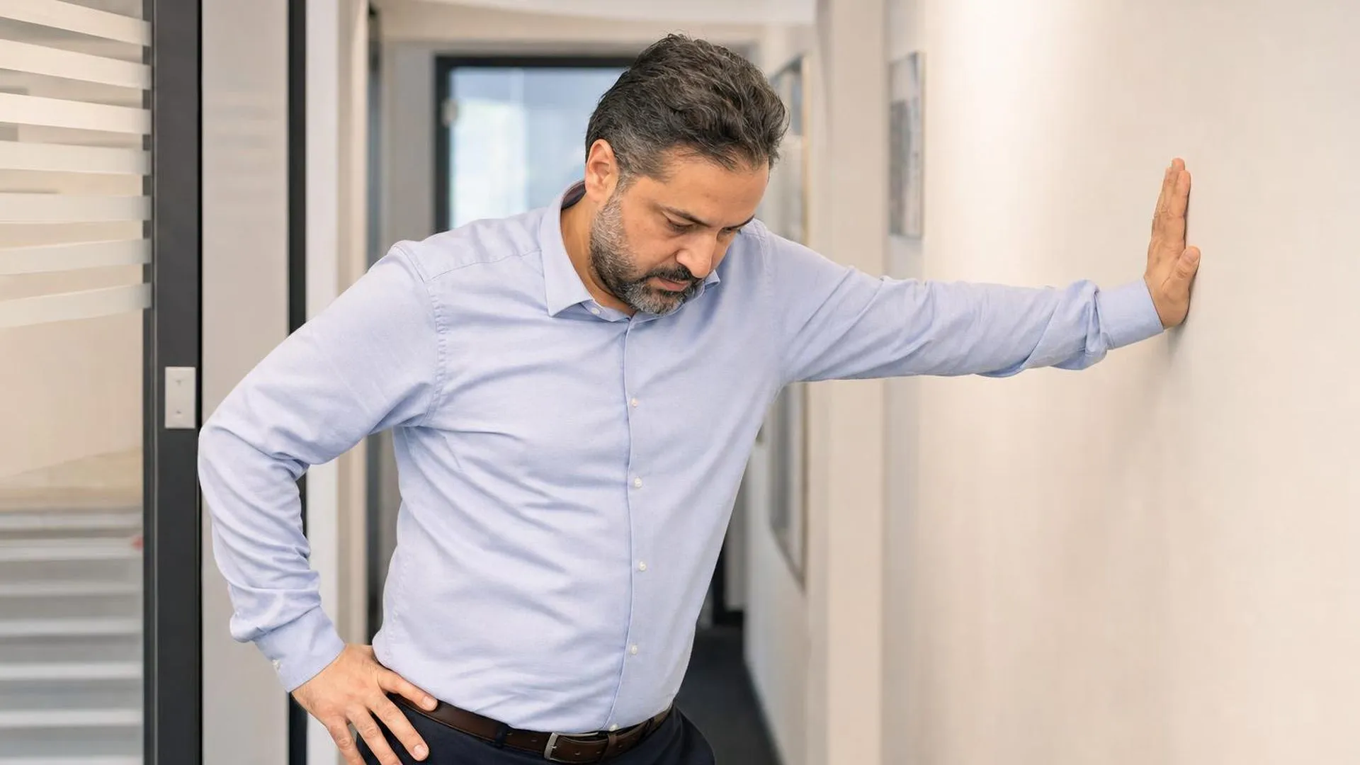Persoon die even pauzeert in een kantoorgang, hand tegen de muur