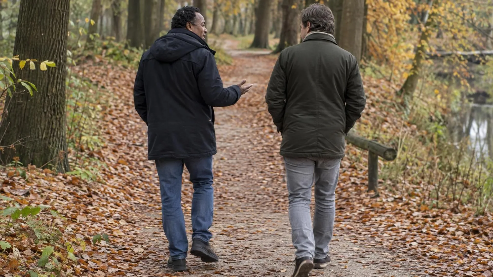 Twee vrienden wandelen pratend over een bospad vol herfstbladeren.
