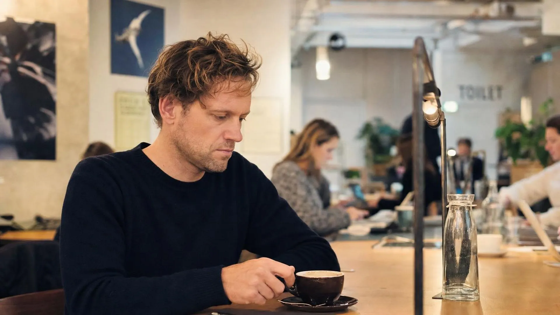 Persoon zit peinzend aan een tafel in een café en staart naar zijn koffie