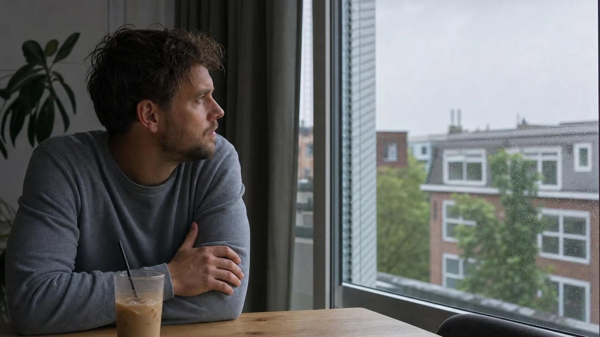 Persoon aan tafel met koud kopje koffie, starend naar buiten