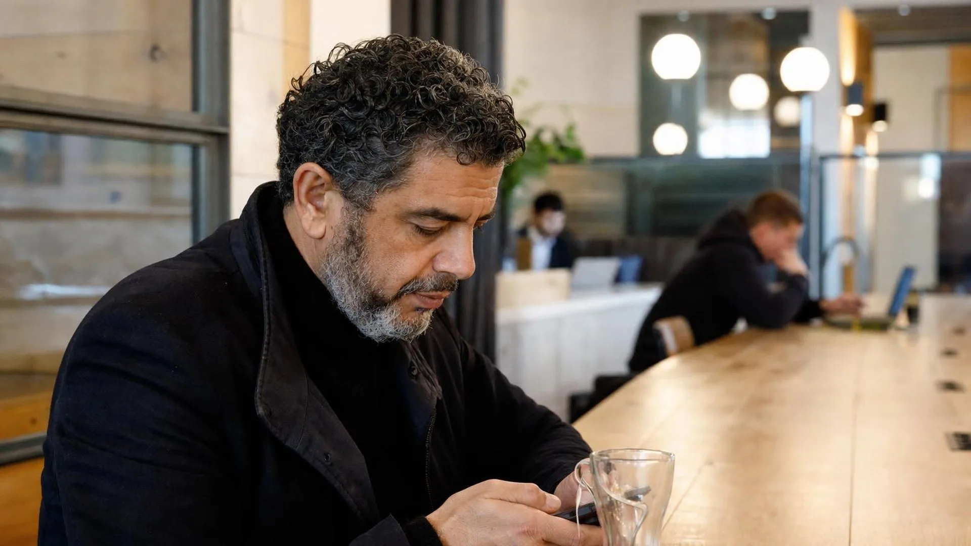 Persoon zit alleen aan een grote tafel en kijkt naar beneden, zichtbaar gespannen
