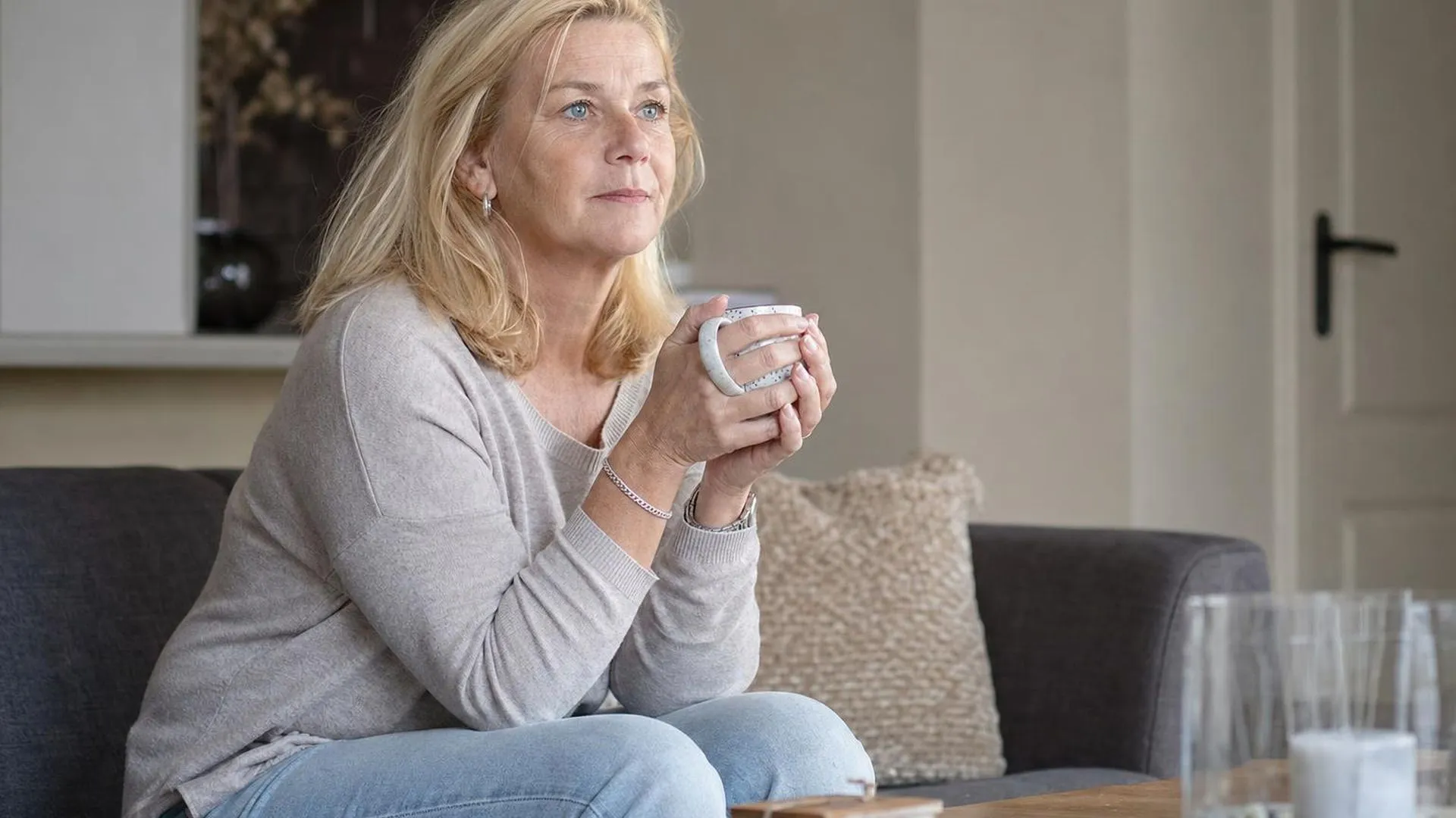 Persoon zit stil op de bank met een mok in de handen, zichtbaar vermoeid