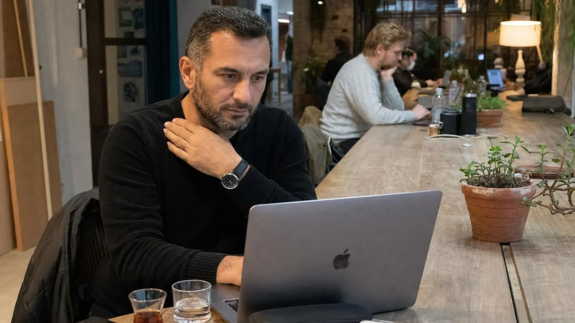 Persoon aan werktafel met hand op borst, afgeleid van het scherm