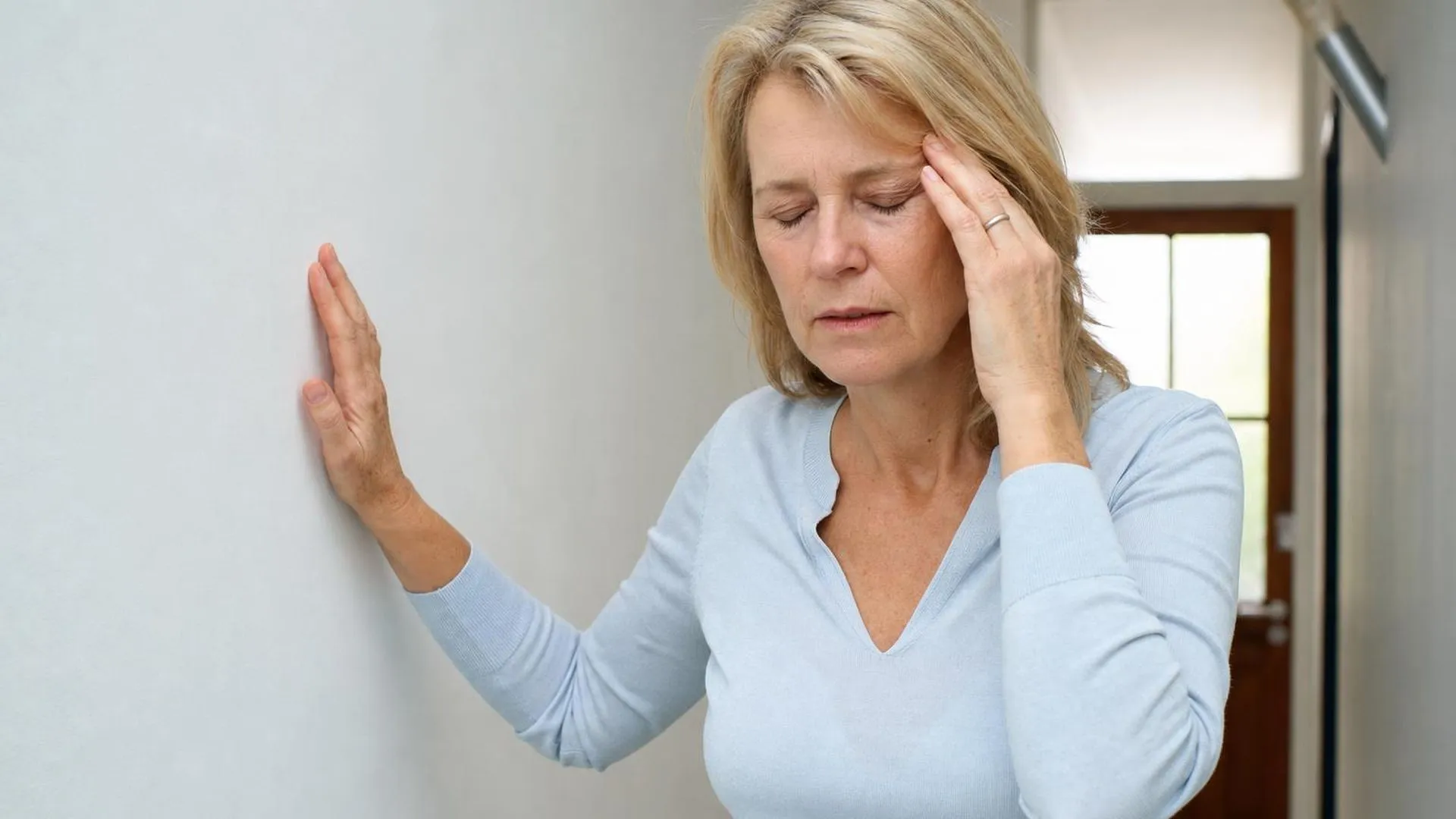Persoon leunt uitgeput tegen een muur in een gang