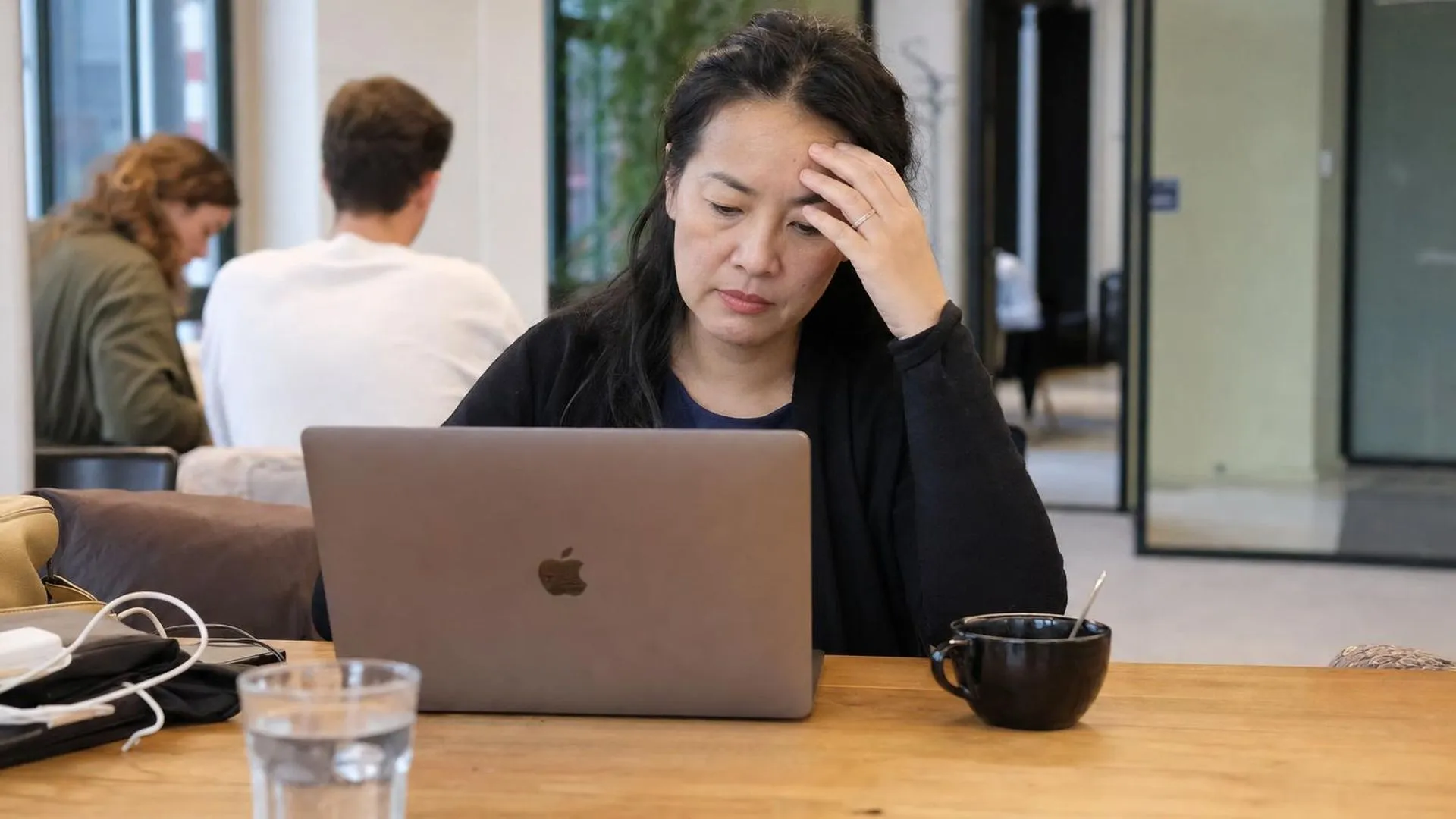 Persoon die moeizaam nadenkt door stress achter een laptop in een koffiebar