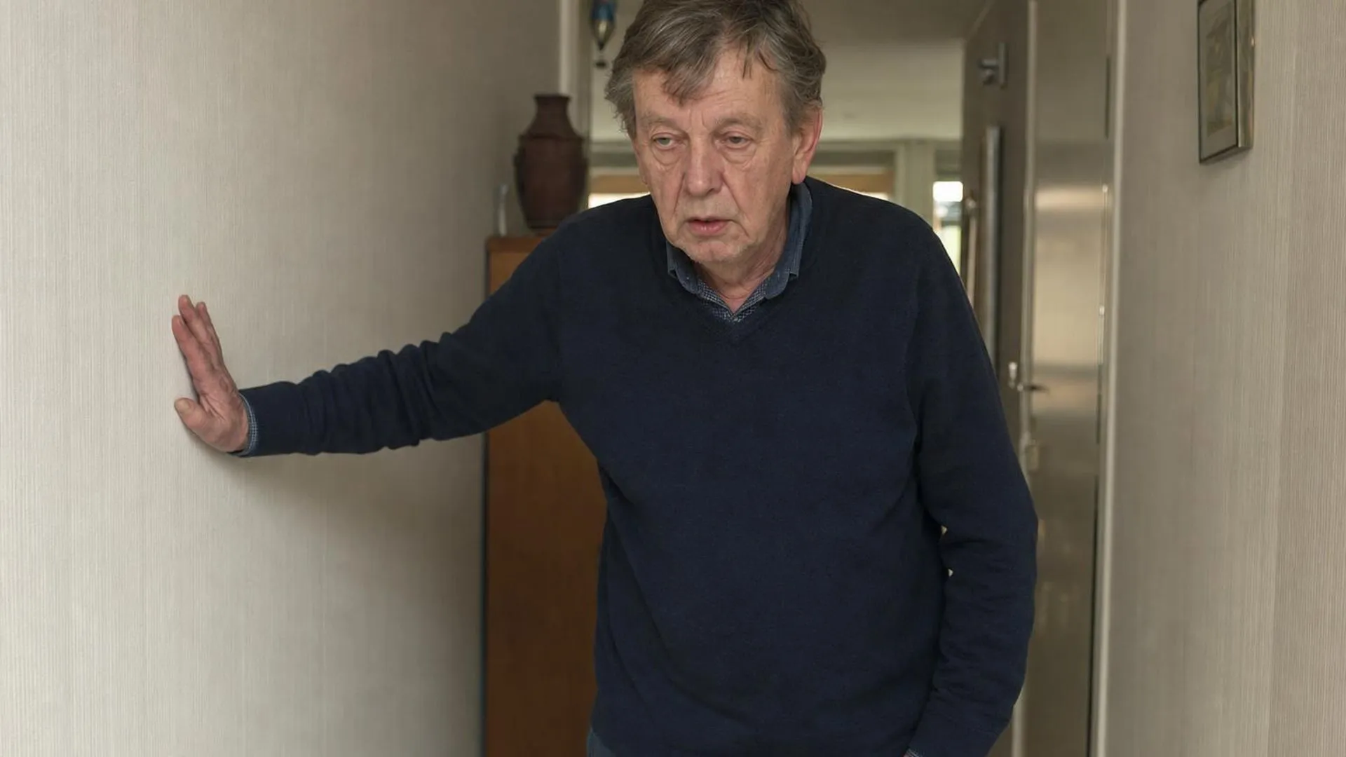 Persoon die even pauze neemt in een gang, hand tegen de muur