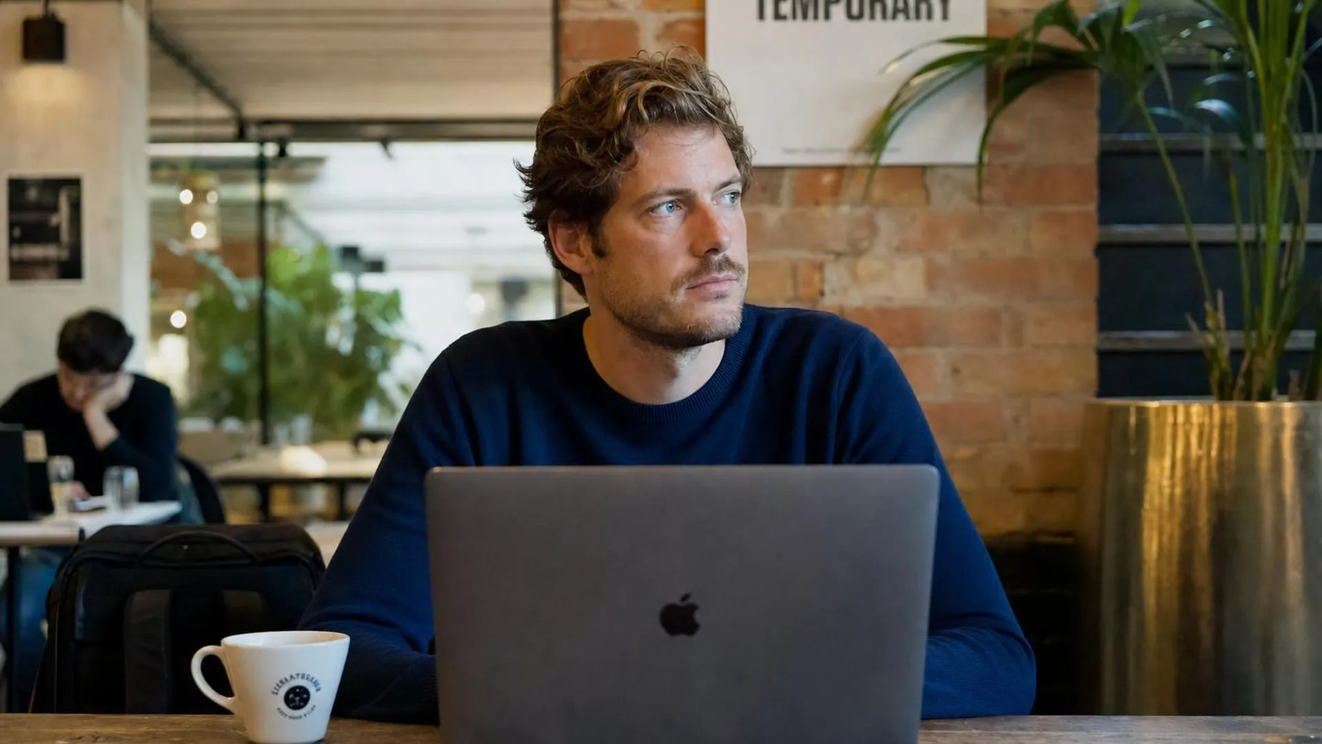 Iemand staart langs een laptopscherm heen in een café, zichtbaar afgeleid en gespannen