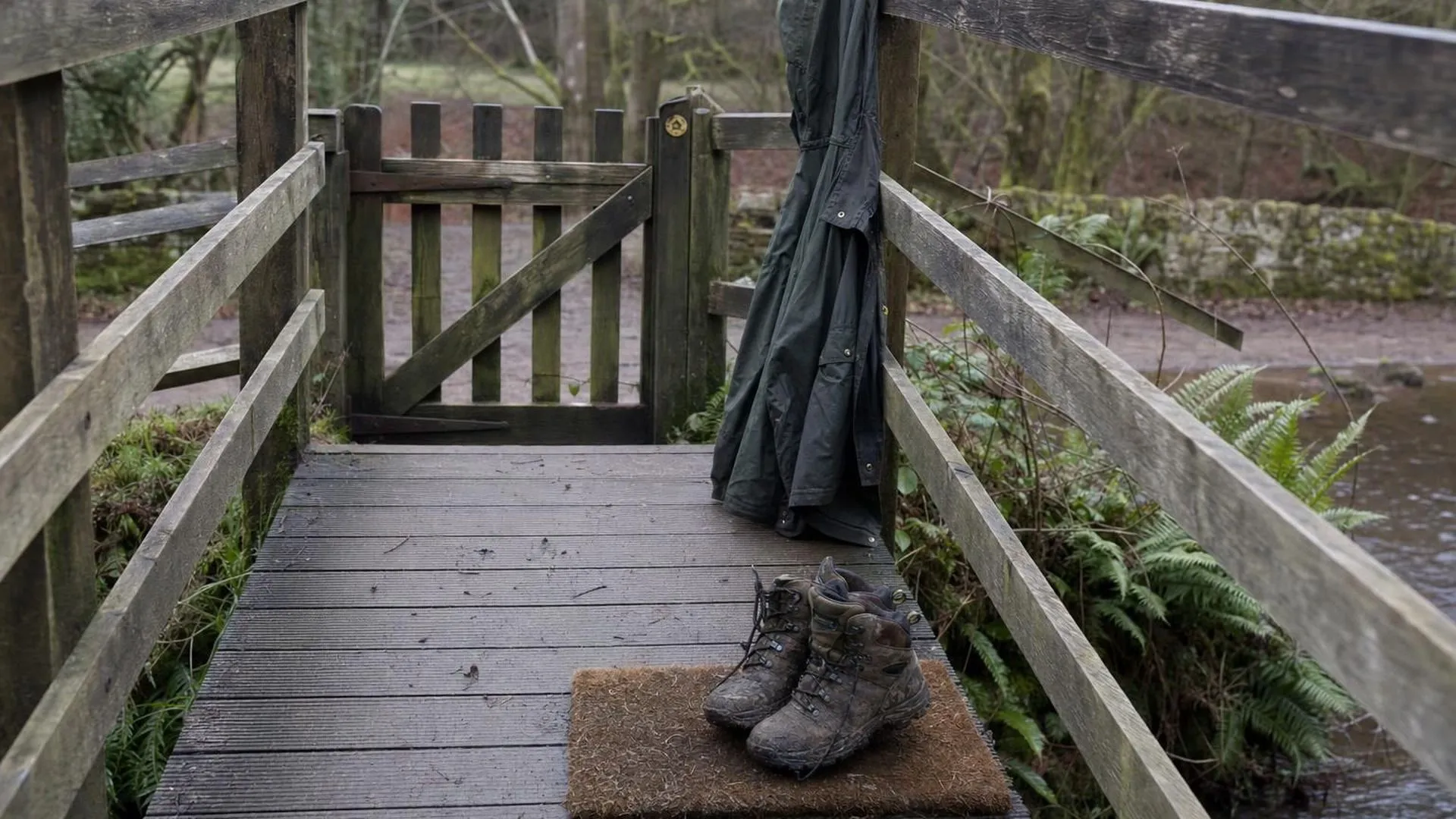 Modderige wandelschoenen op een deurmat naast een jas aan de kapstok