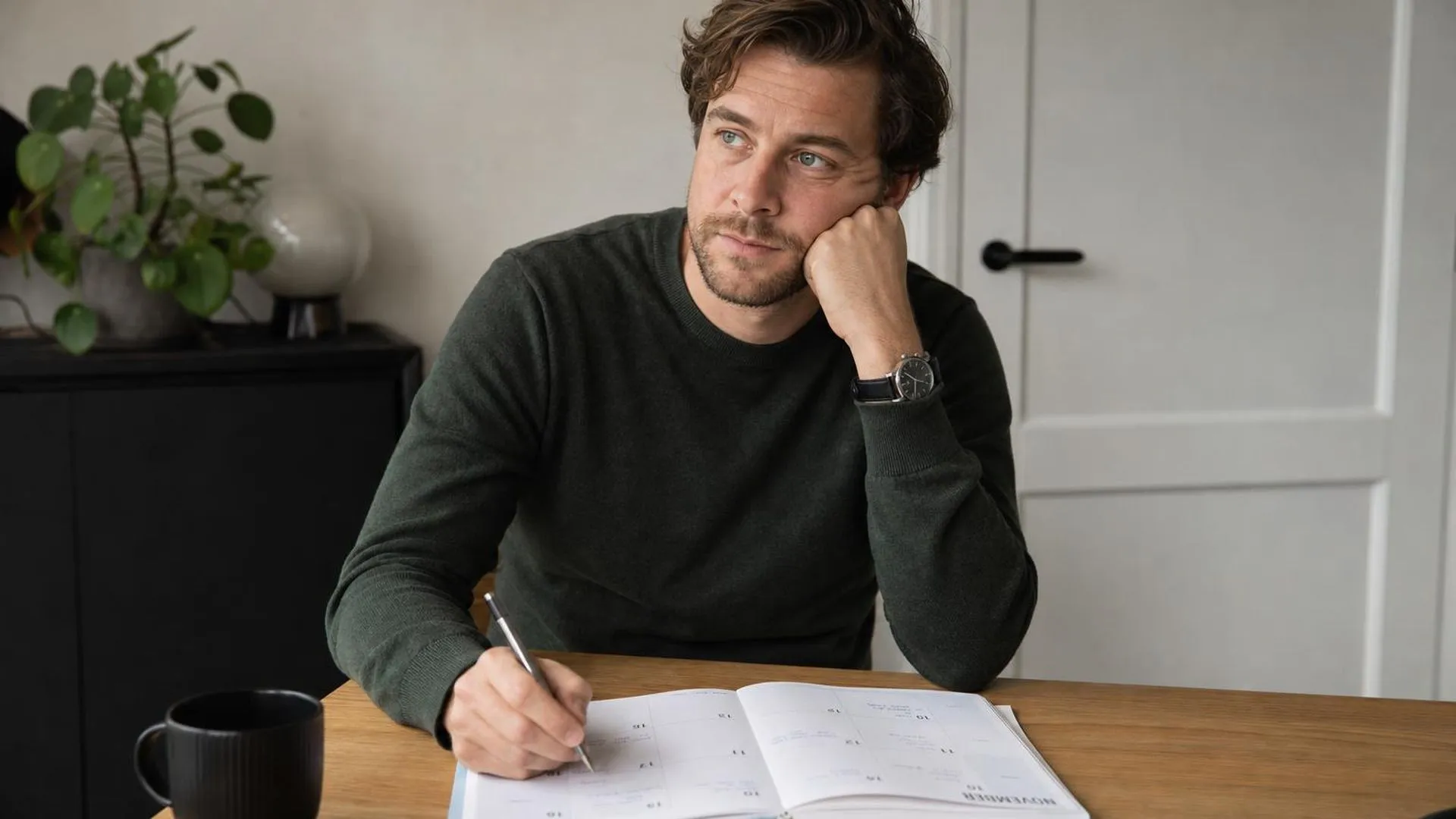Persoon die een weekplanning invult aan een eettafel met zachte verlichting