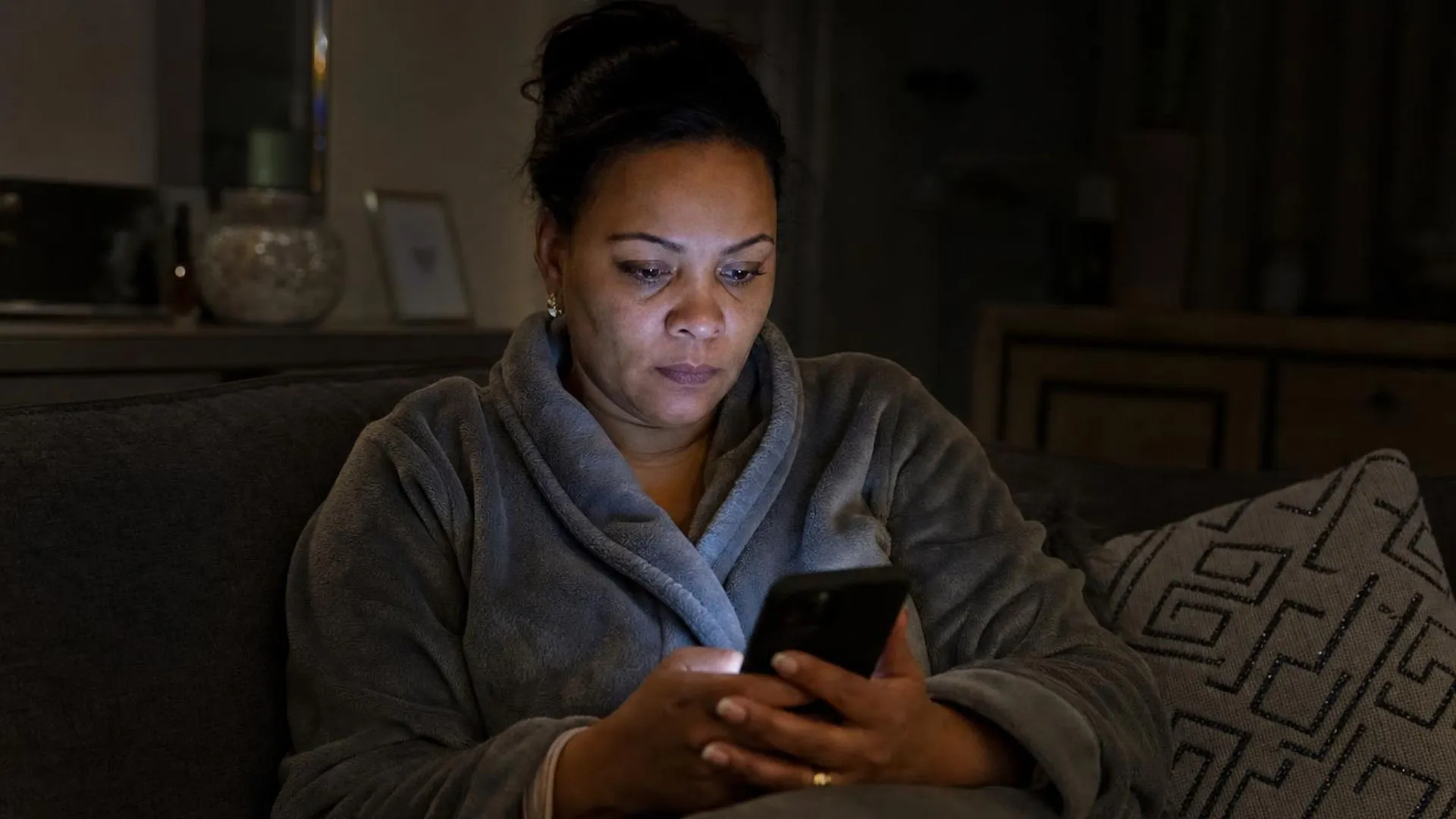 Persoon zit laat op de avond op de bank met telefoon in de hand