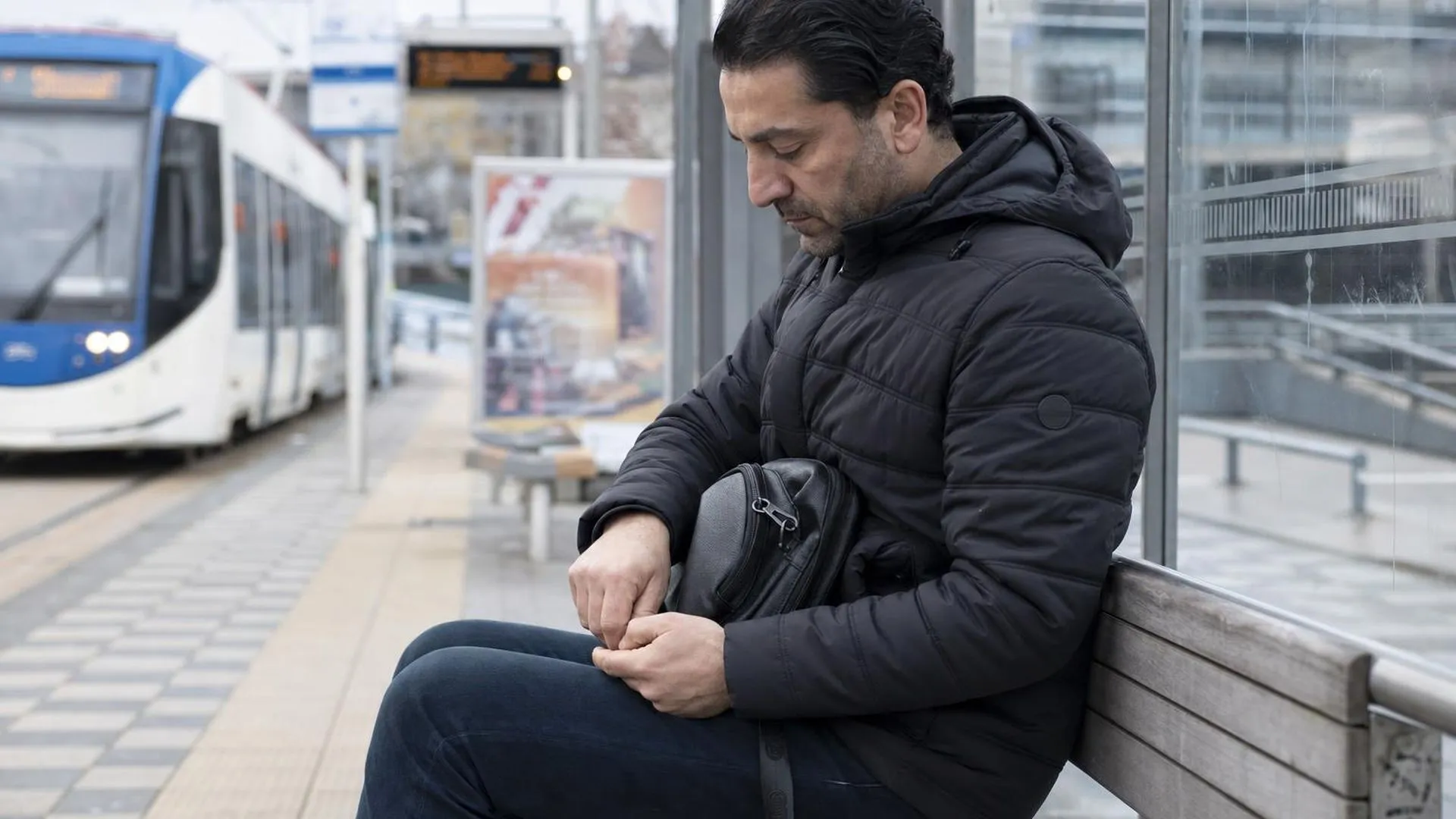 Persoon zit op een bankje op een tramstation en kijkt naar de grond